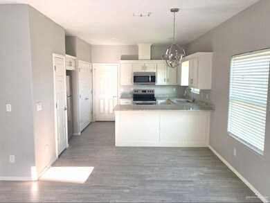 Kitchen with light stone countertops, a peninsula, stainless steel appliances, a chandelier, and white cabinets
