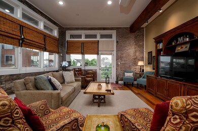 Living room with light wood finished floors, brick wall, beamed ceiling, recessed lighting, and a high ceiling