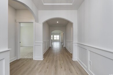 Corridor with light wood-type flooring, arched walkways, a wainscoted wall, a decorative wall, and recessed lighting