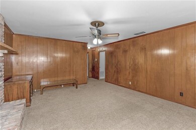 Unfurnished living room featuring light colored carpet, ceiling fan, ornamental molding, and wooden walls