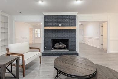 Living area with a decorative wall, built in shelves, a brick fireplace, light wood-type flooring, and crown molding
