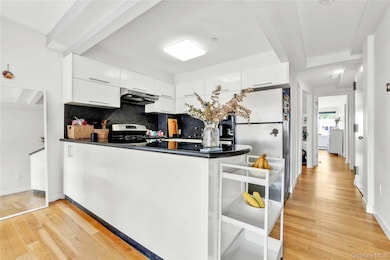 Kitchen featuring a peninsula, tasteful backsplash, white cabinets, light wood-type flooring, and dark stone countertops