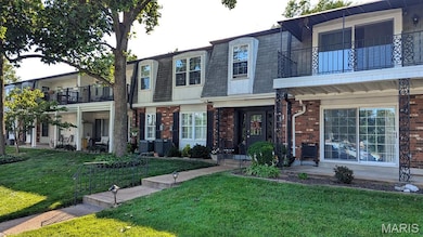 View of front of property featuring a balcony, mansard roof, brick siding, and a front lawn