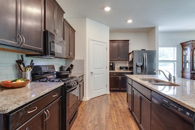 Kitchen with black appliances, dark brown cabinets, light wood finished floors, light stone countertops, and recessed lighting