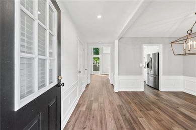 Foyer entrance with dark wood finished floors, a chandelier, wainscoting, and a decorative wall