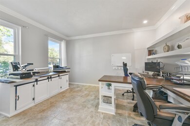 Opposite the dining room, a pair of French doors open into this private study that features crown molding, recessed lighting, tile floors, a pair of front-facing windows, and a custom built-in dual desk station with drawers,  shelving, and a center peninsula.