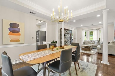 Dining room with crown molding, dark wood-type flooring, ornate columns, recessed lighting, and a chandelier
