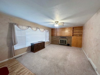 Unfurnished living room featuring built in shelves, a glass covered fireplace, a textured ceiling, light carpet, and ceiling fan