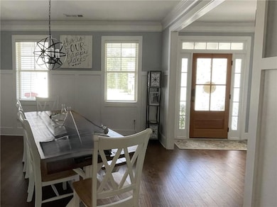 Dining room featuring a chandelier, dark wood-style floors, a wainscoted wall, ornamental molding, and a decorative wall