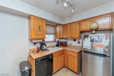 Kitchen with stainless steel fridge, track lighting, light tile floors, black dishwasher, and sink