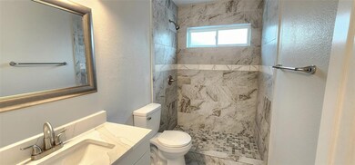 Bathroom featuring a tile shower, vanity, and toil