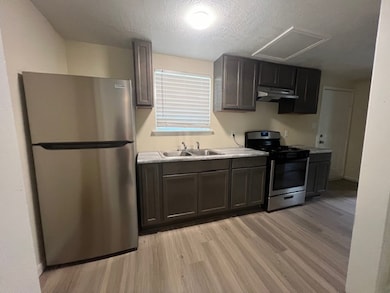 Kitchen with stainless steel appliances, light wood-style flooring, light countertops, a textured ceiling, and under cabinet range hood
