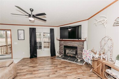 Living room featuring ornamental molding, a stone fireplace, light wood-style floors, ceiling fan, and a textured ceiling