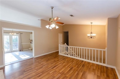 Unfurnished room featuring a chandelier, a ceiling fan, hardwood finished floors, lofted ceiling, and french doors
