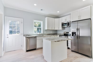 Kitchen featuring a kitchen island, light stone counters, sink, white cabinetry, and appliances with stainless steel finishes