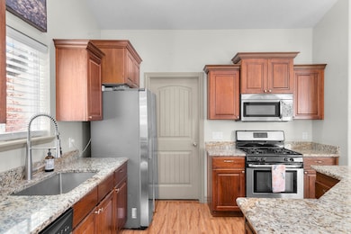 Kitchen featuring stainless steel appliances, light wood-style flooring, light granite countertops, and gas stove.