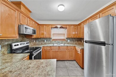 Kitchen with appliances with stainless steel finishes, sink, light stone countertops, tasteful backsplash, and light tile floors