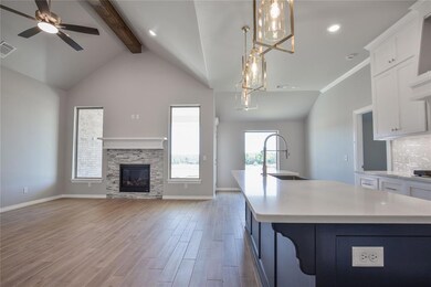 Kitchen with hanging light fixtures, an island with sink, sink, and a fireplace