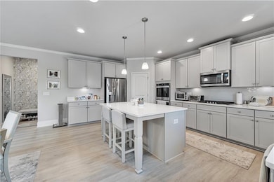 Kitchen featuring crown molding, gray cabinets, tasteful backsplash, a kitchen bar, and decorative light fixtures
