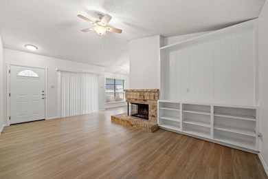 Unfurnished living room featuring light wood-type flooring, a textured ceiling, a fireplace, and ceiling fan