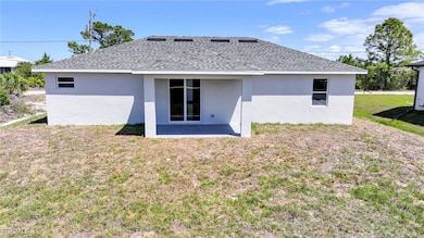 Rear view of house with roof with shingles, stucco siding, a yard, and a patio area