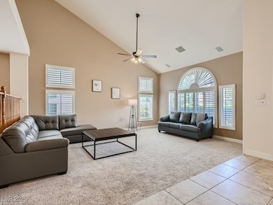 Family room with high vaulted ceiling, light tile patterned floors, light carpet, shutters, and a ceiling fan with light