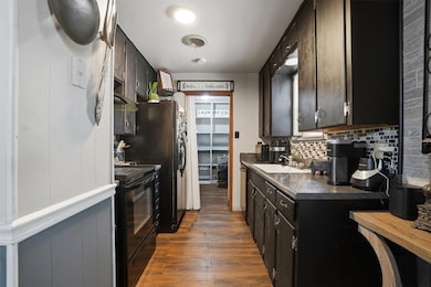 Kitchen featuring dark countertops, dark wood finished floors, black appliances, backsplash, and dark cabinetry