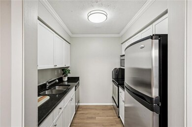 Kitchen with stainless steel appliances, crown molding, a textured ceiling, light wood finished floors, and dark stone countertops