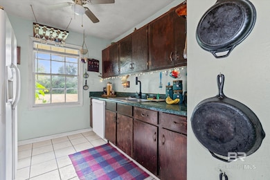 Kitchen with dark countertops, dark brown cabinetry, light tile patterned flooring, white appliances, and ceiling fan