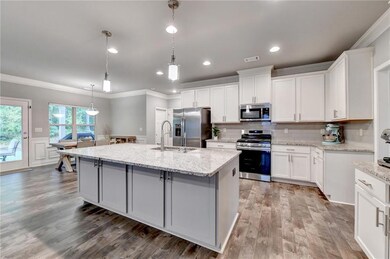 Kitchen with wood finished floors, an island with sink, appliances with stainless steel finishes, ornamental molding, and visible vents
