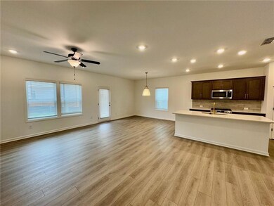 Kitchen with stainless steel microwave, light countertops, light wood-type flooring, dark brown cabinets, and open floor plan