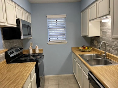 Kitchen with stainless steel appliances, decorative backsplash, a textured wall, light tile patterned floors, and light countertops