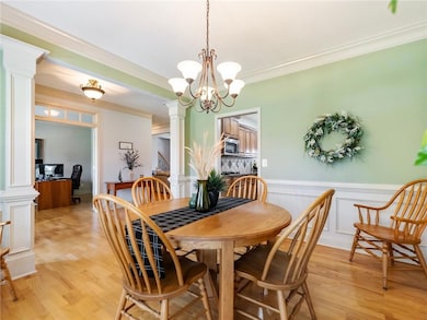 Dining area with ornate columns, light wood-style flooring, ornamental molding, a chandelier, and wainscoting