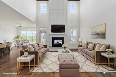 Living area featuring wood finished floors, healthy amount of natural light, a high ceiling, and a multi sided fireplace
