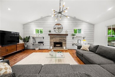 Living room with plenty of natural light, a chandelier, lofted ceiling, wood finished floors, and wooden walls
