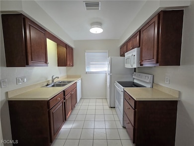Kitchen featuring white appliances, light countertops, light tile patterned floors, and dark brown cabinetry