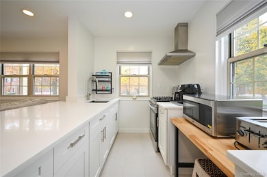 Kitchen featuring recessed lighting, wall chimney range hood, stainless steel appliances, white cabinets, and light stone countertops