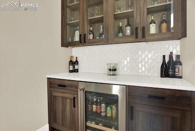 Indoor dry bar featuring wine cooler and tasteful backsplash