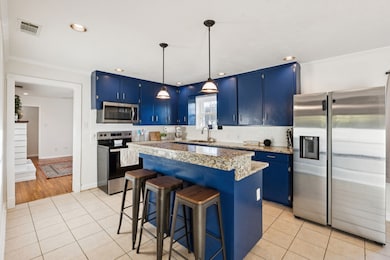 Kitchen with blue cabinets, a kitchen bar, pendant lighting, stainless steel appliances, and light tile patterned floors