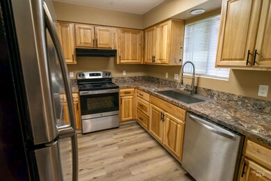 Kitchen with stainless steel appliances, under cabinet range hood, light wood finished floors, dark countertops, and a textured ceiling