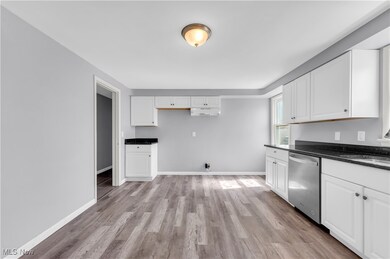 Kitchen with white cabinets, stainless steel dishwasher, dark countertops, and baseboards