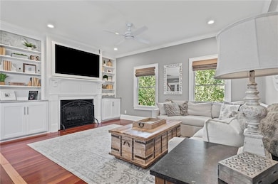 Living room featuring wood finished floors, crown molding, recessed lighting, a gas fireplace, and built ins.