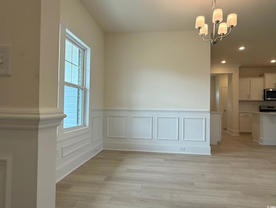 Unfurnished dining area featuring a chandelier, light wood-type flooring, recessed lighting, and wainscoting
