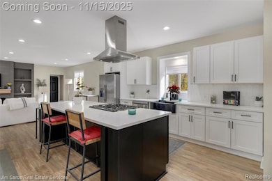 Kitchen featuring open floor plan, island range hood, white cabinets, a kitchen breakfast bar, and light wood-type flooring