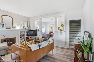 Living area with wood finished floors, a fireplace, decorative columns, and a chandelier