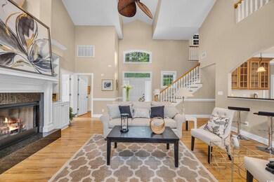 Living area with wood finished floors, stairs, a towering ceiling, a fireplace, and baseboards