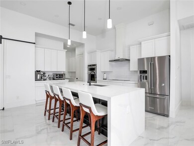Kitchen featuring light marble finish flooring, appliances with stainless steel finishes, a breakfast bar, light countertops, and an island with sink