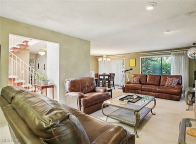 Living area with a chandelier, light carpet, a textured ceiling, and stairway