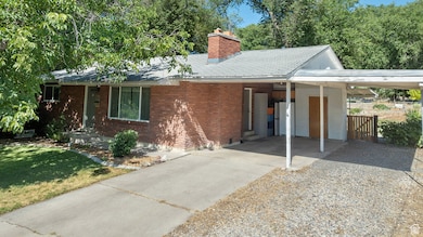 Ranch-style home with driveway, a chimney, a carport, a shingled roof, and brick siding