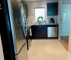Kitchen featuring appliances with stainless steel finishes, dark cabinetry, tasteful backsplash, and light countertops